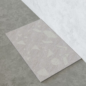 Riva shower tray surface showing a bush-hammered stone texture with white marble inlay shapes (triangles, circles and curved forms), with light-catching water droplets.