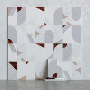 Tratti marble tile samples featuring geometric inlay motifs (semi-circles and triangles) in white and grey stone with deep red veined marble accents, arranged on a grey surface.
